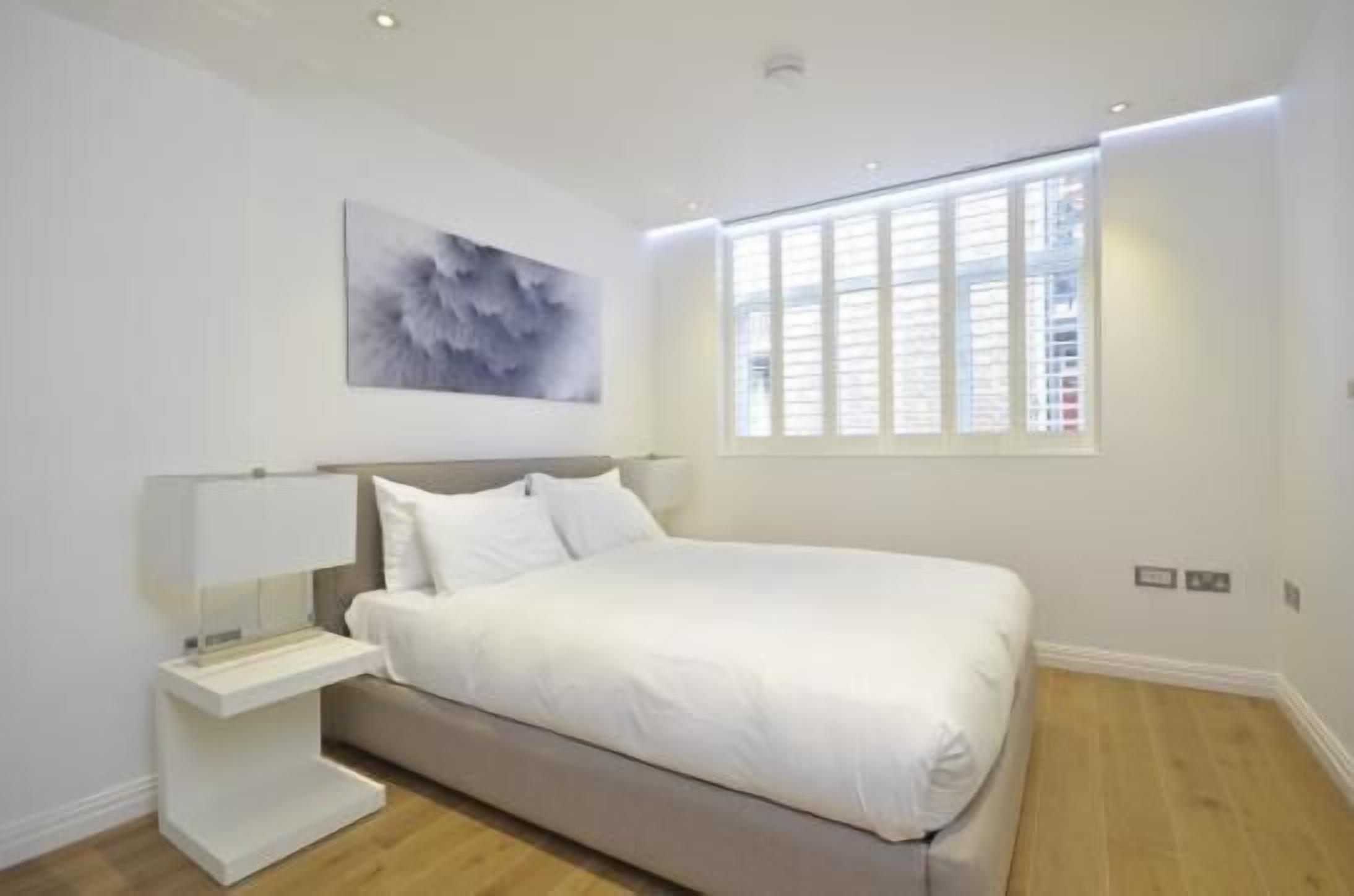 Een moderne slaapkamer met een bed, nachtkastje en een raam met jaloezieën.