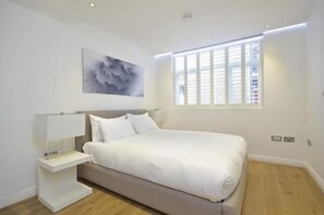 A modern bedroom with a bed, bedside table, and a window with blinds.