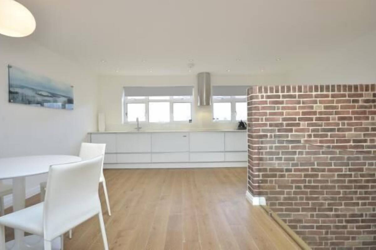 A modern kitchen with white cabinets, a brick accent wall, and a dining area with white chairs.