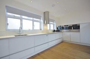 A modern kitchen with white cabinetry, a stainless steel range hood, and a large window providing natural light.