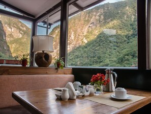 A wooden table with tea set and a view of a mountainous landscape through a window. - Jaya Machupicchu Boutique Hotel (Machu Picchu)