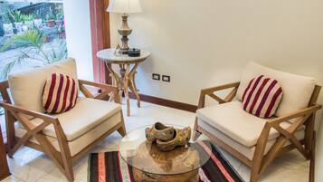 A room with two wooden chairs with striped cushions, a small round table with a lamp, and a decorative wooden bowl.