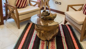 A living room with two wooden chairs, a glass coffee table, a lamp, and a colorful rug.