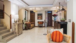 A spacious lobby with a staircase, a sofa, a chair, and a reception desk.