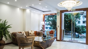 A lobby with a sofa, coffee table, and a wooden chair. There is a chandelier and a sign that reads "SALIDA".