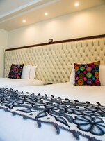 Habitación de hotel con tablero de cabecera acolchado, dos camas y una colcha decorativa.