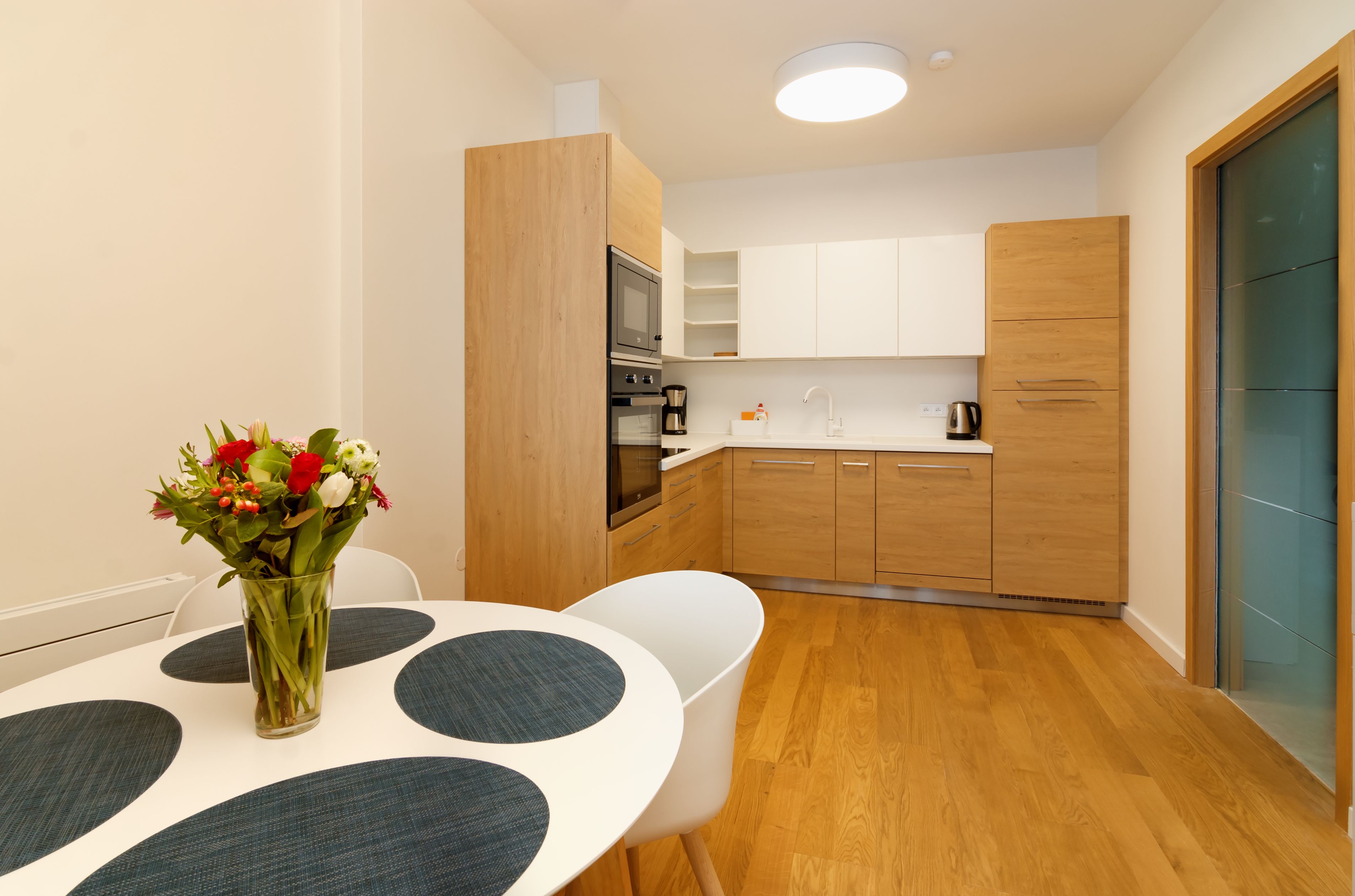 Una cocina moderna con armarios de madera, horno empotrado y comedor con mesa y sillas.