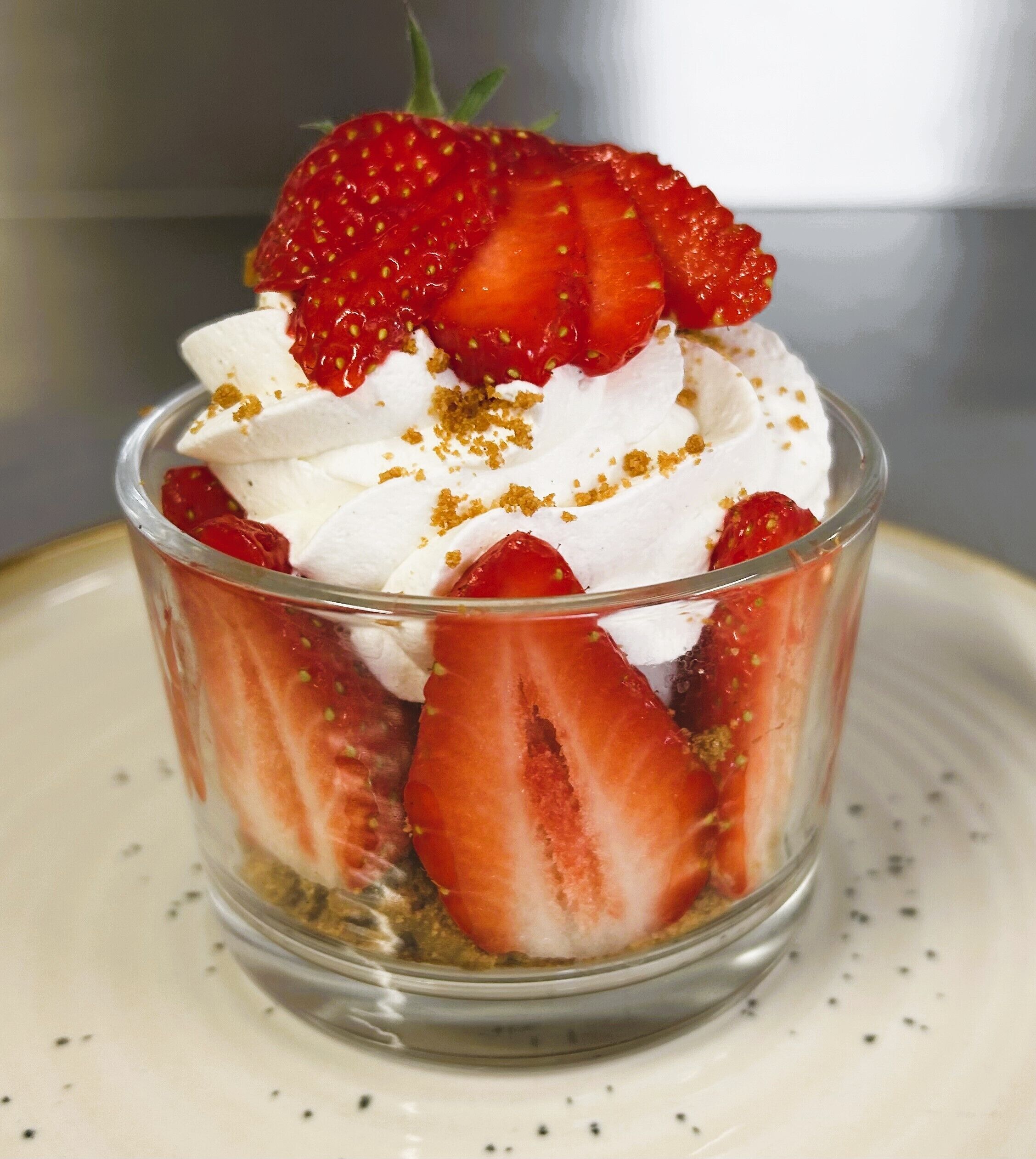 A dessert in a clear glass cup with strawberries and whipped cream.