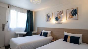 Een hotelkamer met twee bedden, een bureau en een raam met gordijnen.