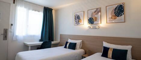 A hotel room with two beds, a desk, and a window with curtains.