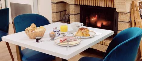 A breakfast setup with a stone fireplace, blue chairs, a white table, and a basket of bread.