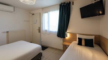 A hotel room with two beds, a TV, a window with curtains, and a radiator.