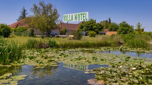 Placa do Hotel Villa, rodeada por um lago com nenúfares e vegetação.