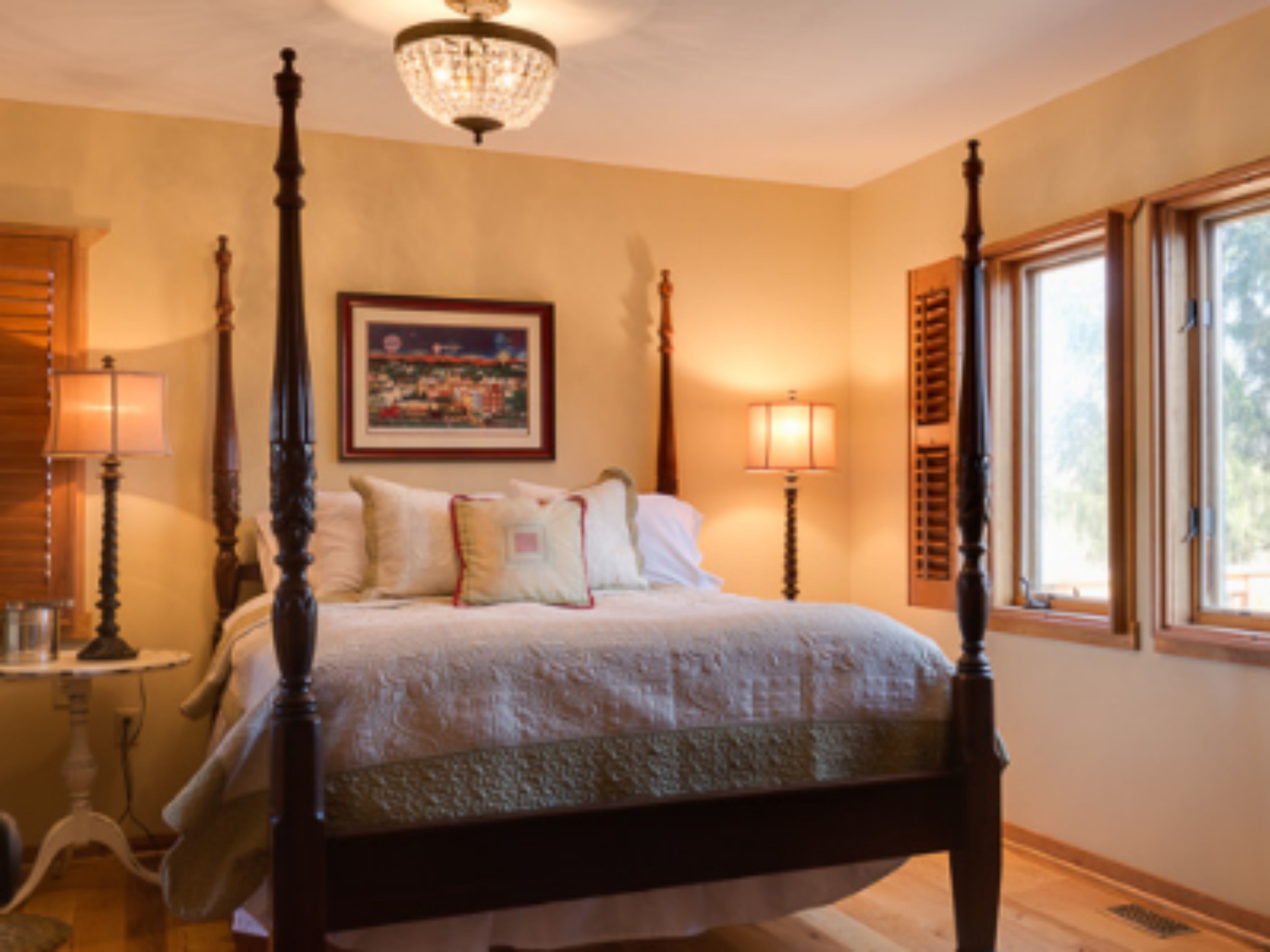 A four-poster bed with a chandelier, bedside lamps, and a framed picture on the wall.