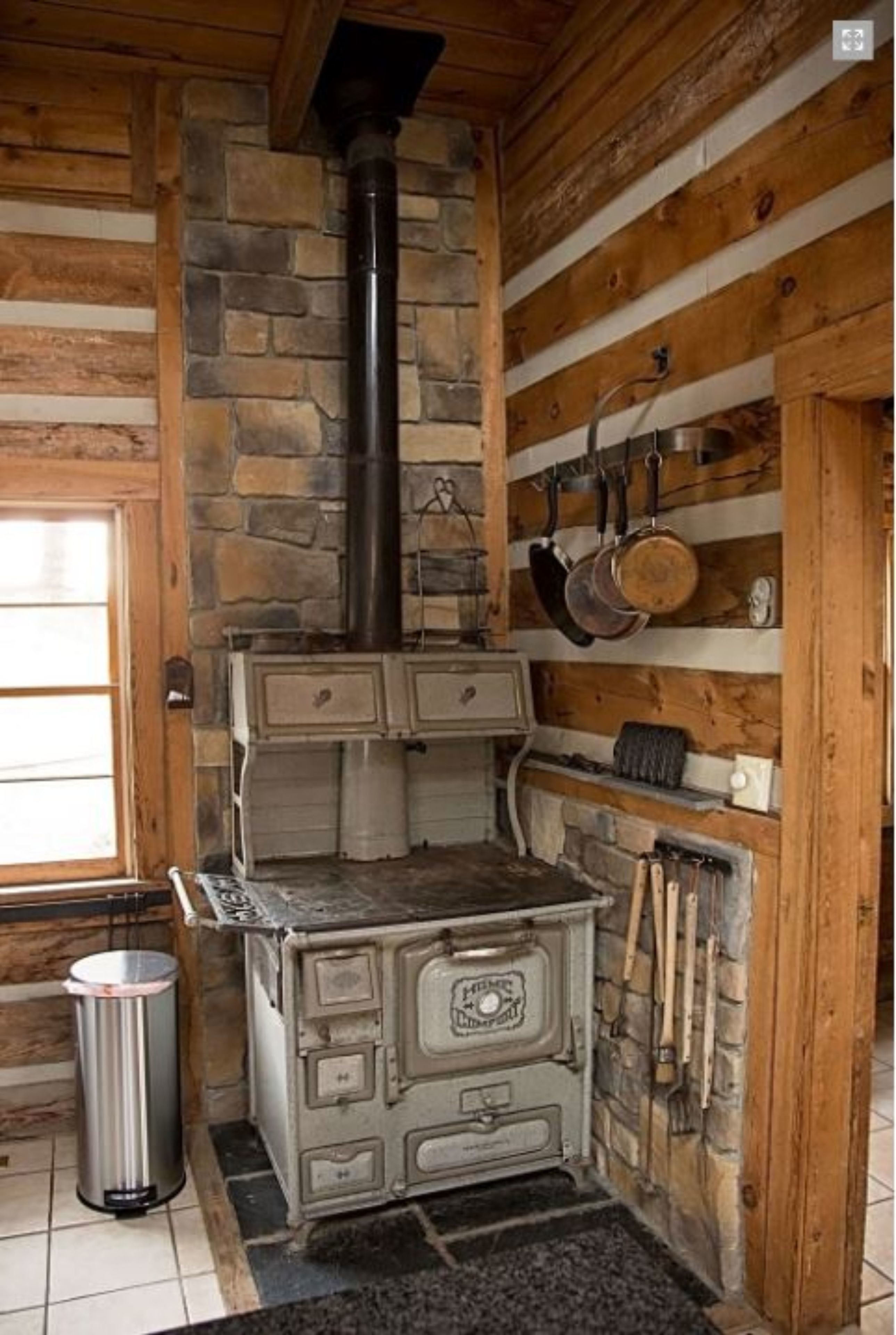 A rustic kitchen with a stone wall, wooden beams, and a vintage stove.