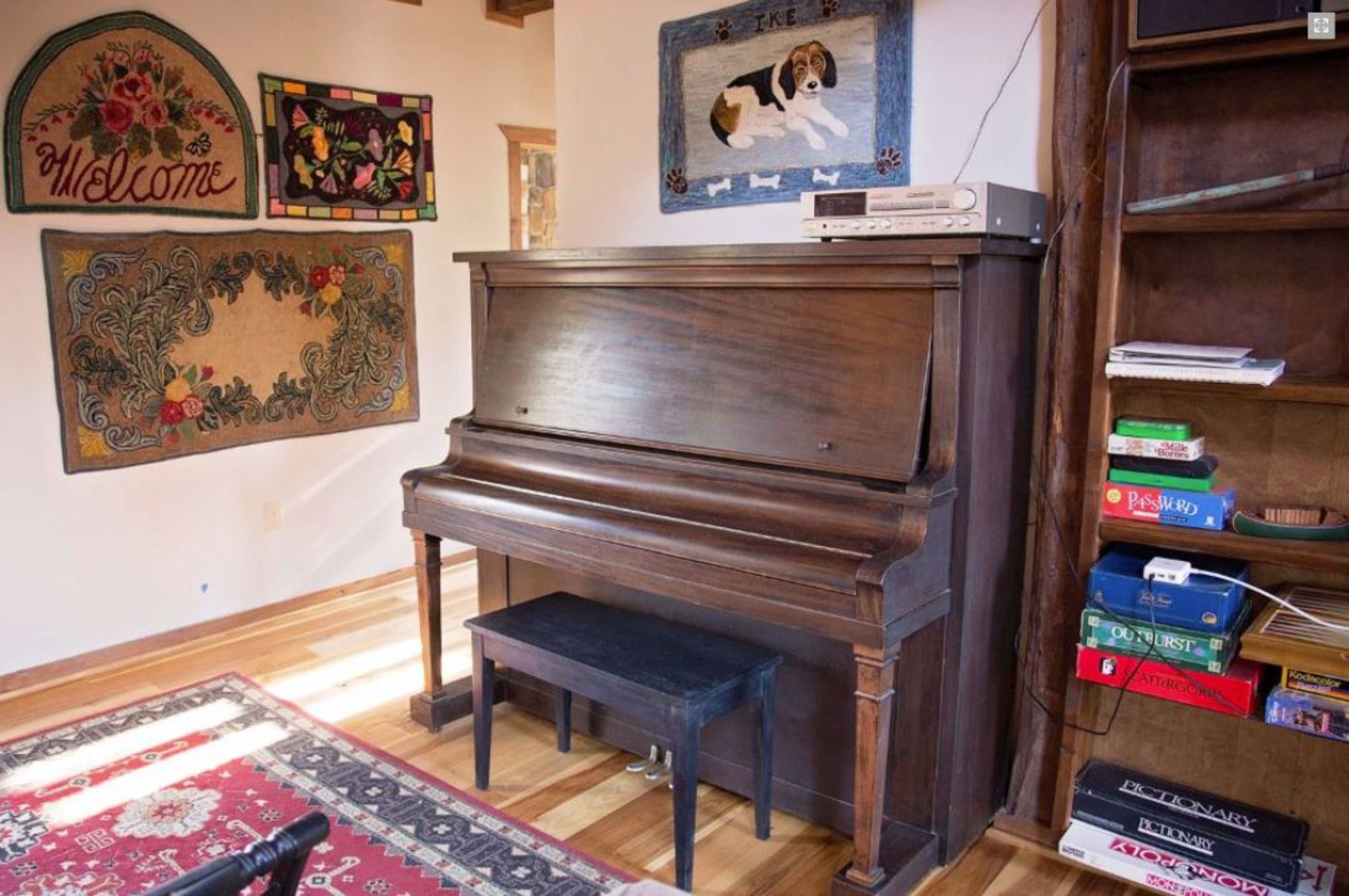 A room with a wooden piano, a bookshelf with books, and decorative wall hangings.