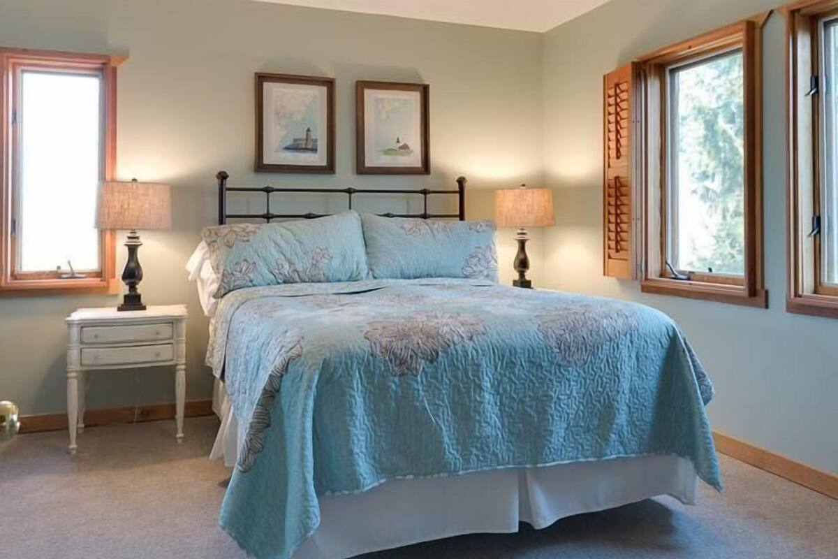 A bedroom with a bed, two bedside tables, two wall-mounted lamps, and two framed pictures.