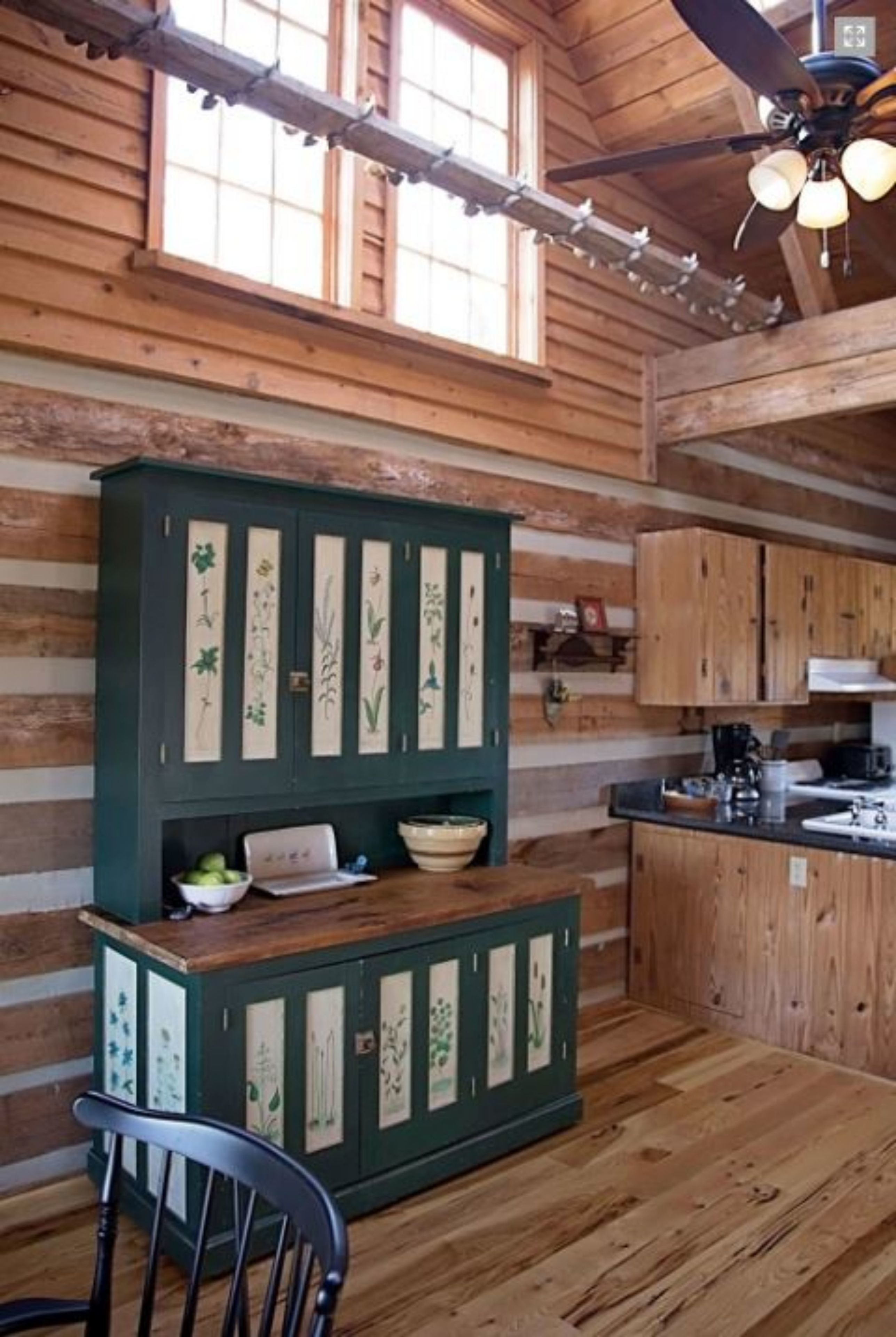A rustic kitchen with wooden cabinets, a central island, and a ceiling fan.