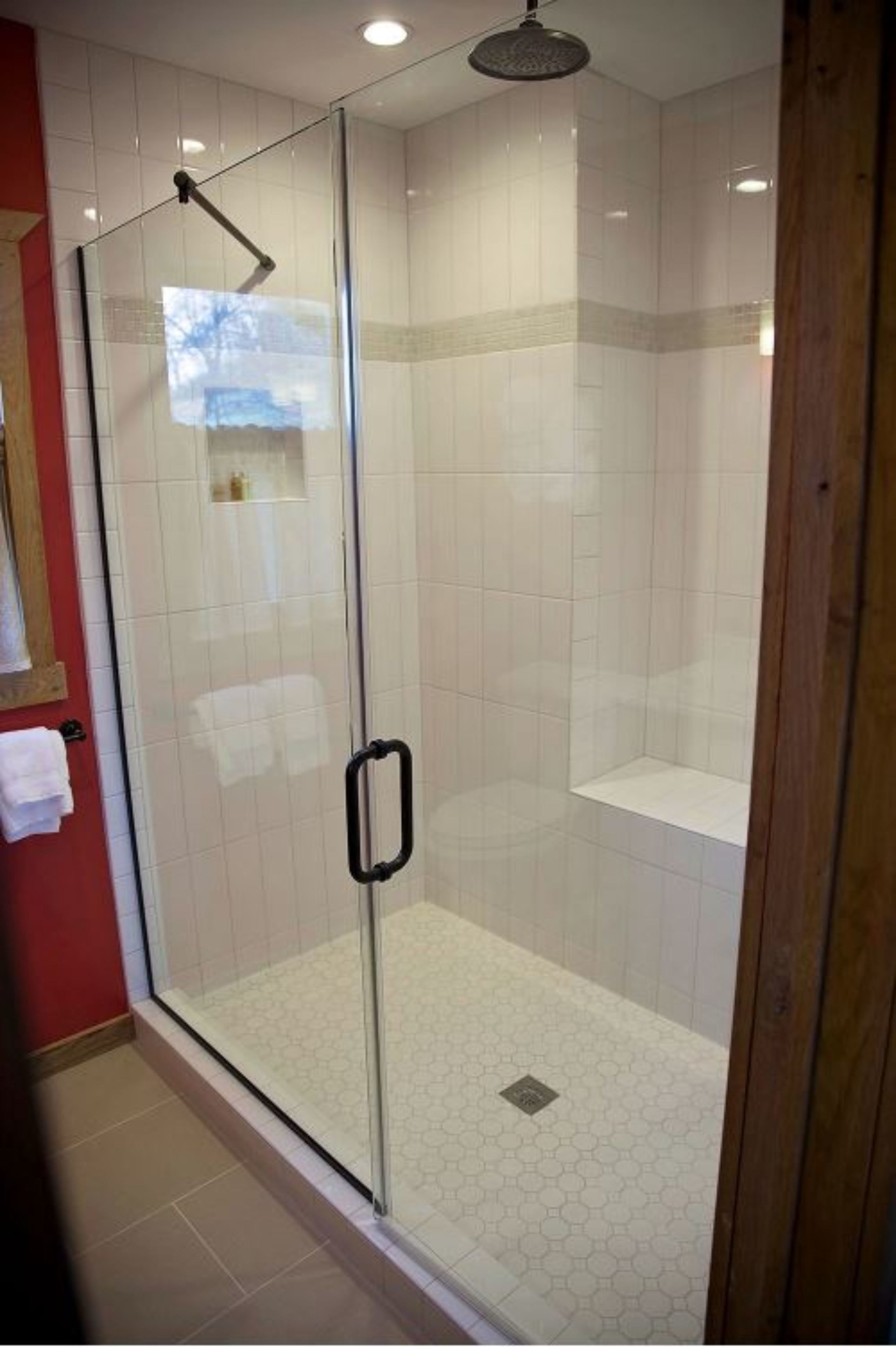 Une douche fermée par des parois de verre, dotée d’un pommeau de douche à effet pluie, de murs carrelés et d’un sol recouvert de carreaux hexagonaux.