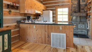 A rustic cabin-style kitchen with wooden walls, a central island, a stove, and a window. - River Bluff Farm Bed & Breakfast (New Market)