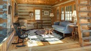 A log cabin interior with a wooden floor, a round table, a blue sofa, and a rocking chair. - River Bluff Farm Bed & Breakfast (New Market)
