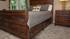 A wooden bed with a headboard, grey bedding, and a nightstand with drawers. - Red Fox Run B&B (Cazenovia)