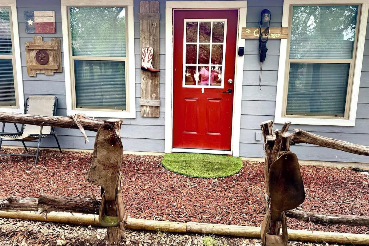 A house with a red door, wooden porch, and a small garden area with mulch and a green lawn.