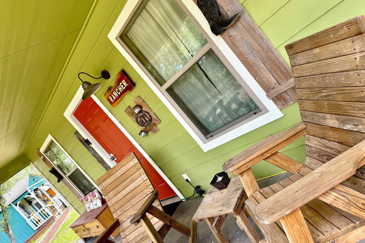 A rustic cabin with a green exterior, a red door, and a window with a wooden frame.