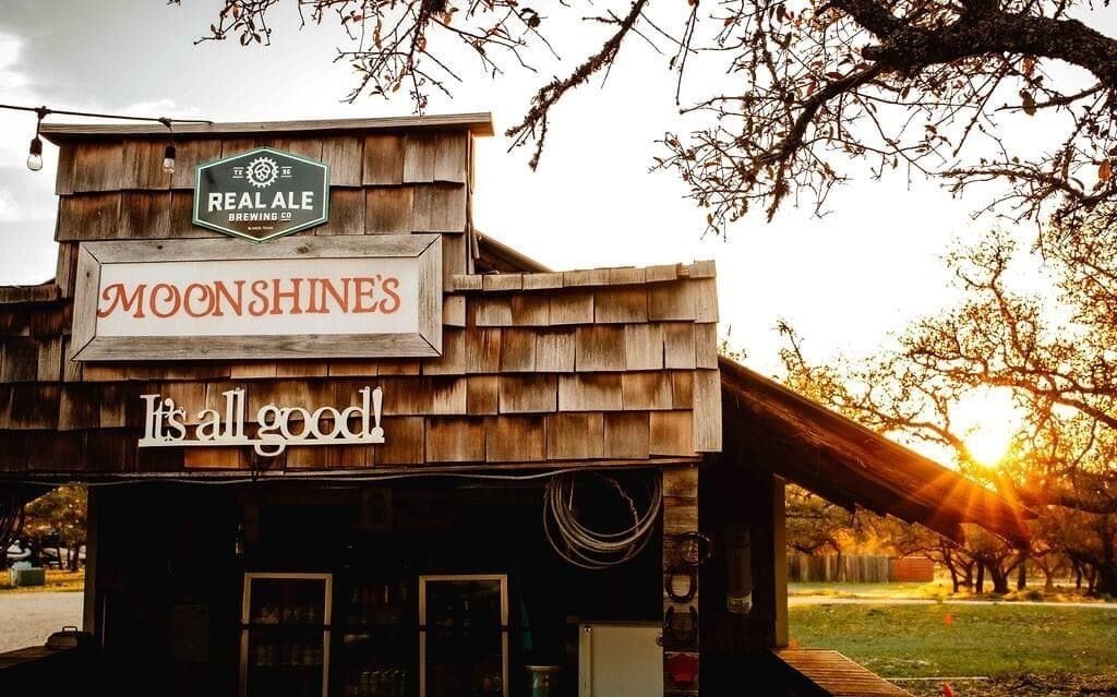 A rustic building with a sign that reads "MOONSHINES" and "It's all good."
