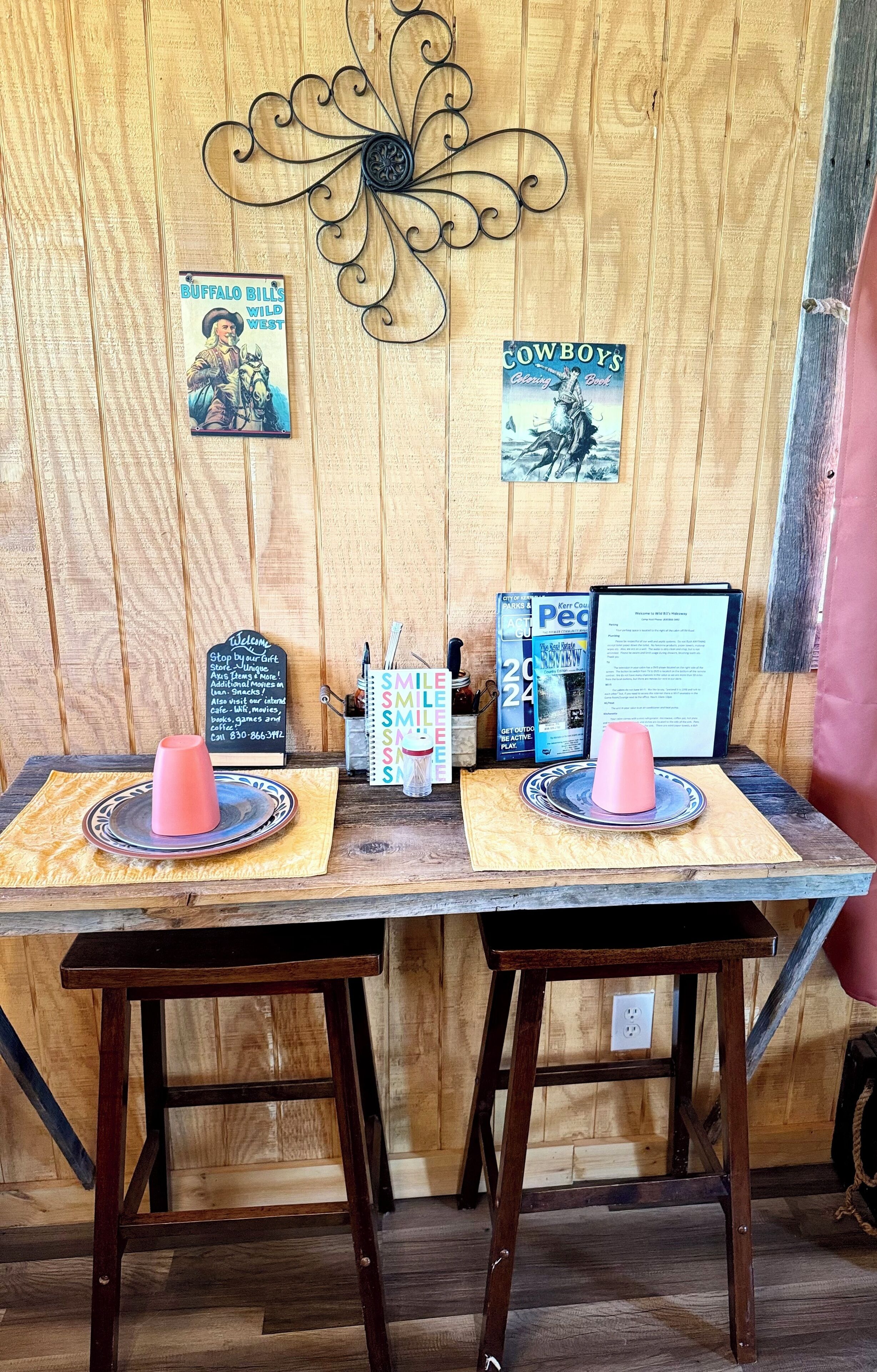 A rustic wooden table with two stools, a decorative metal piece, and vintage posters.
