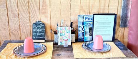 Een rustieke houten tafel met twee krukken, een decoratief metalen object en oude posters.