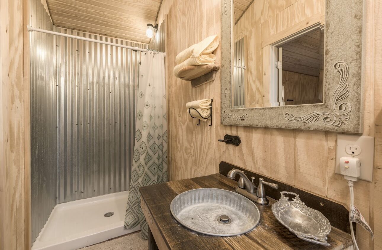 A bathroom with a wooden vanity, a large mirror, and a shower with a metal door.