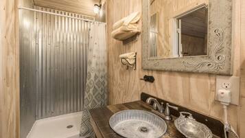 A bathroom with a wooden vanity, a large mirror, and a shower with a metal door.
