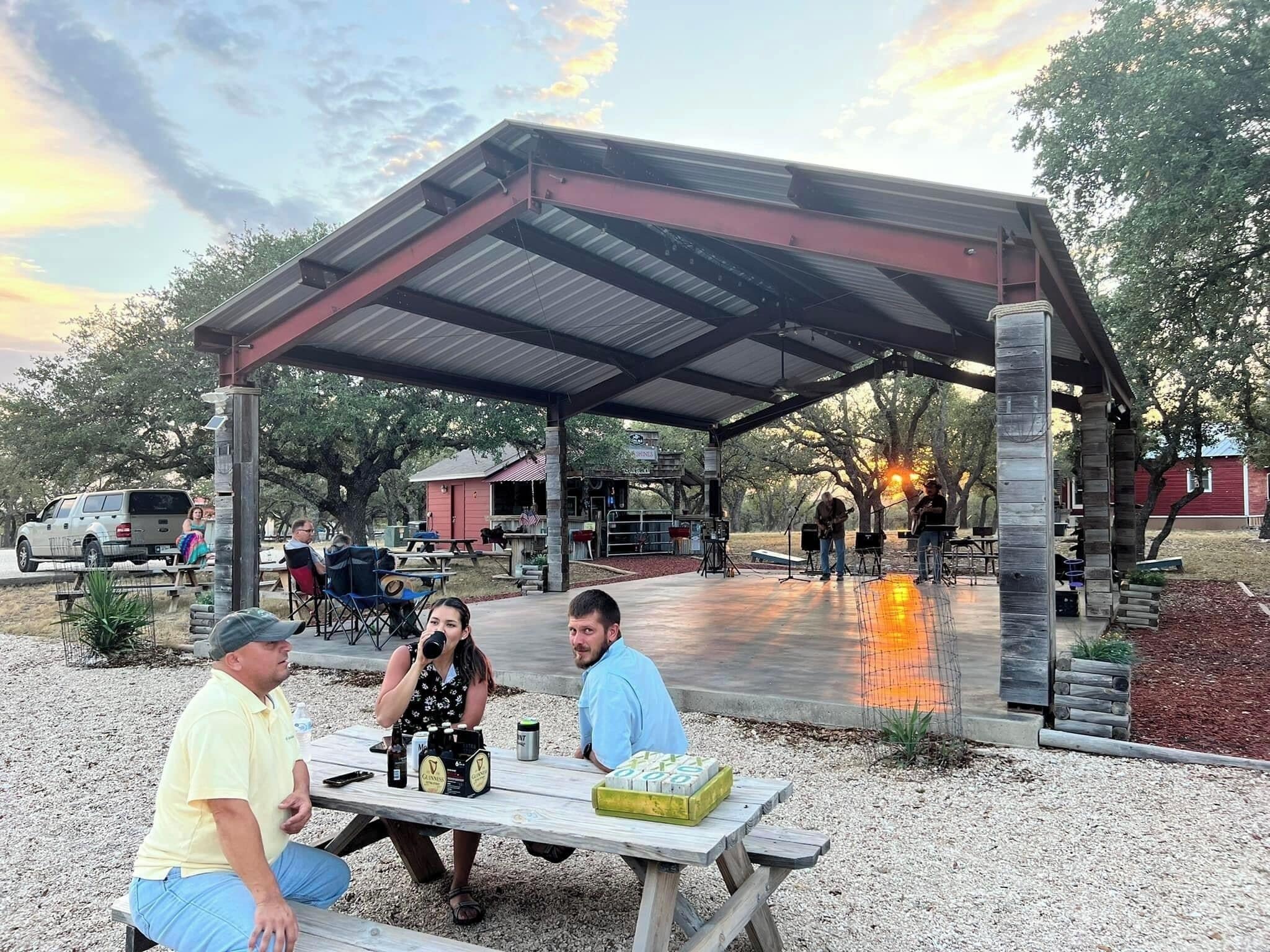 An outdoor patio area with a covered seating area, picnic tables, and a stage for performances.