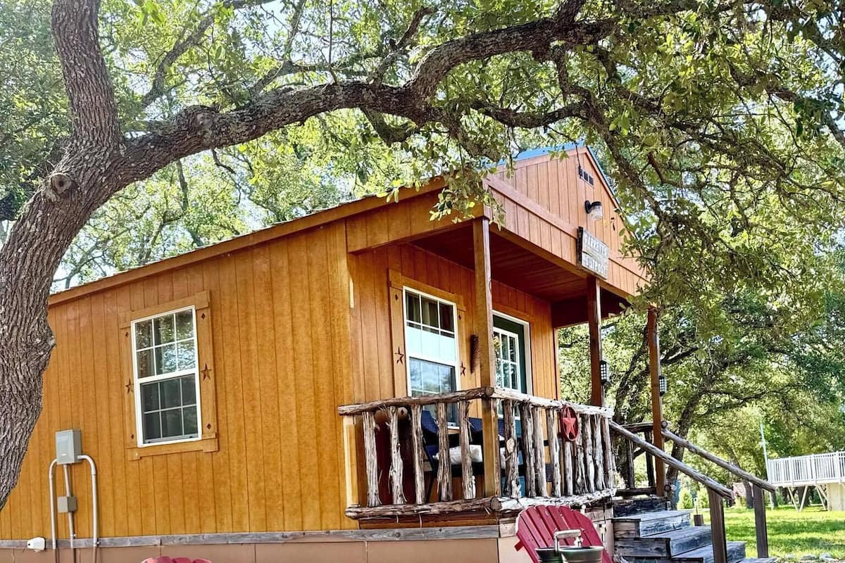 A wooden cabin with a porch, a table, and red Adirondack chairs.