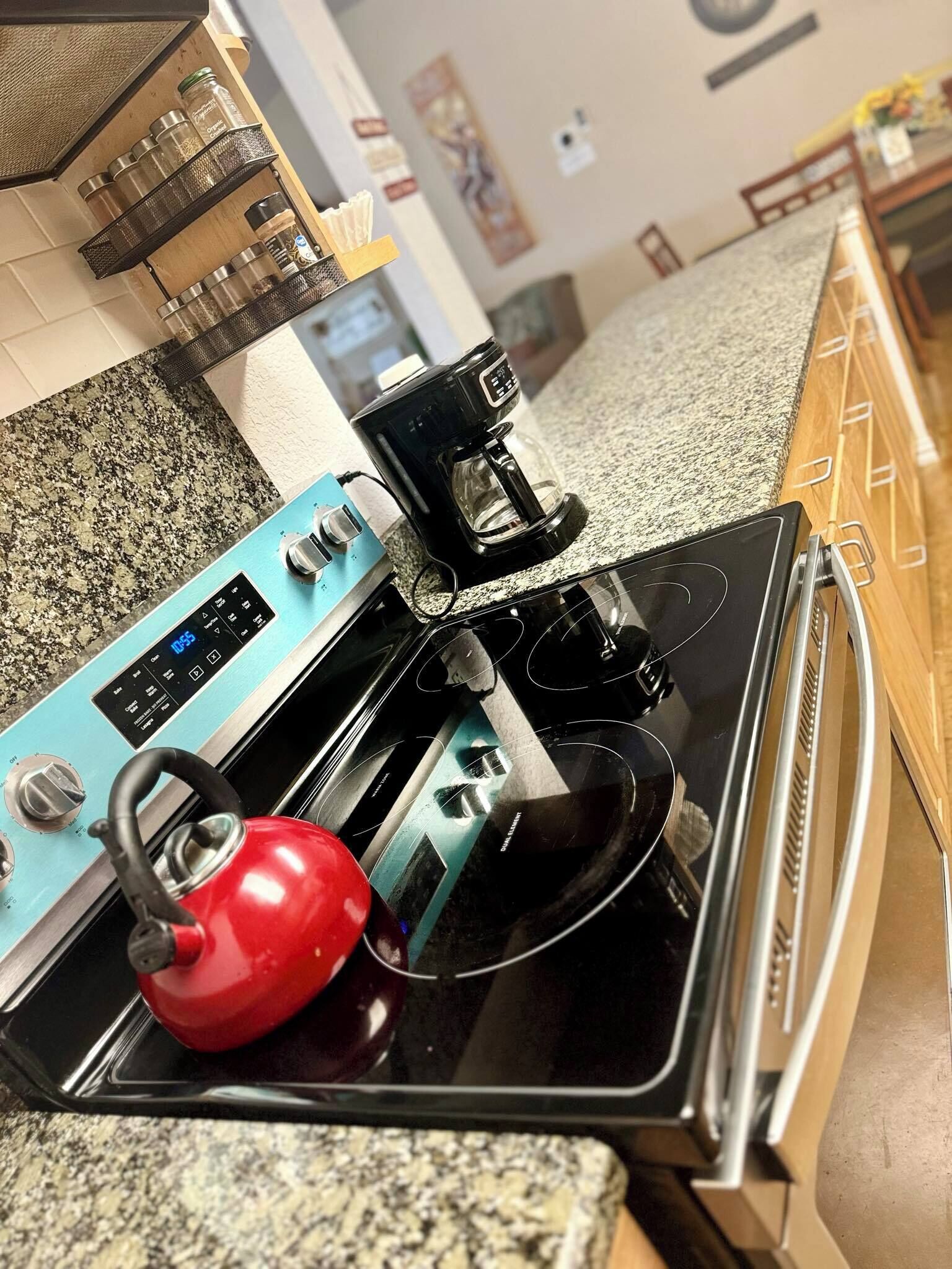 Una cocina con una estufa azul, un hervidor rojo y una cafetera sobre la encimera.
