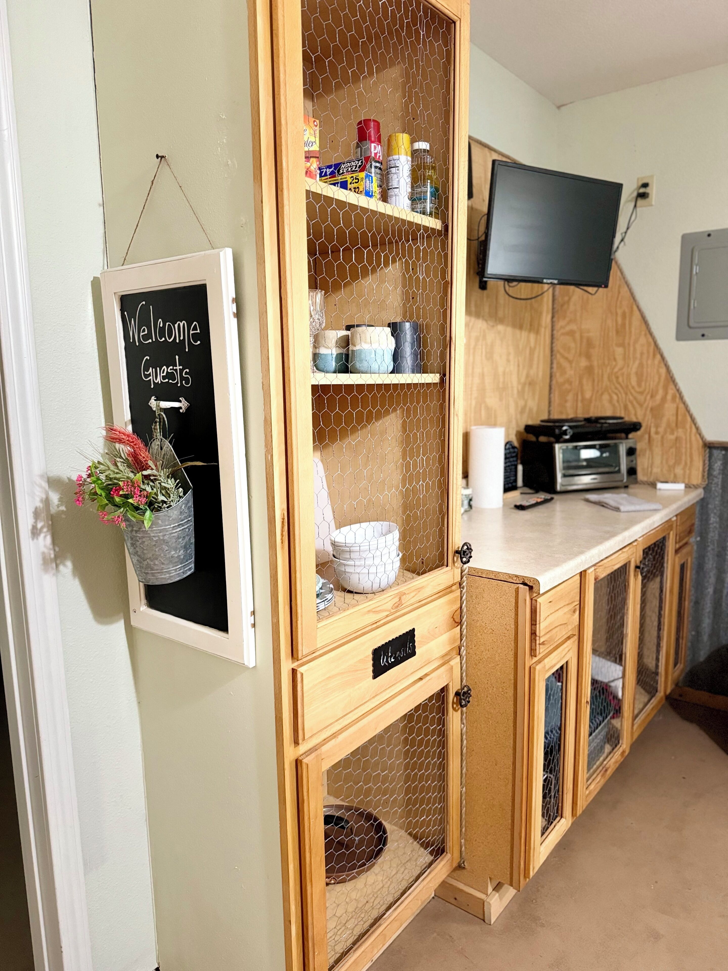 A kitchen with a wooden cabinet, a welcome sign, a TV, and a microwave.