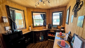 Una cucina accogliente in stile baita, con pareti e pavimenti in legno, un'isola centrale con lavello e un tavolo da pranzo con una tazza e un piattino rossi.