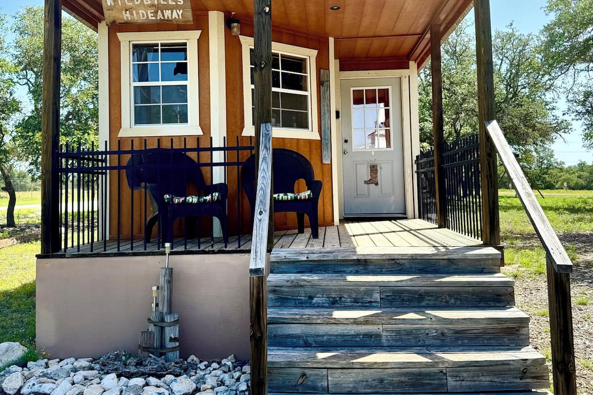 A rustic hideaway with a wooden exterior, a porch with two chairs, and a sign reading "Wildbills Hideaway."