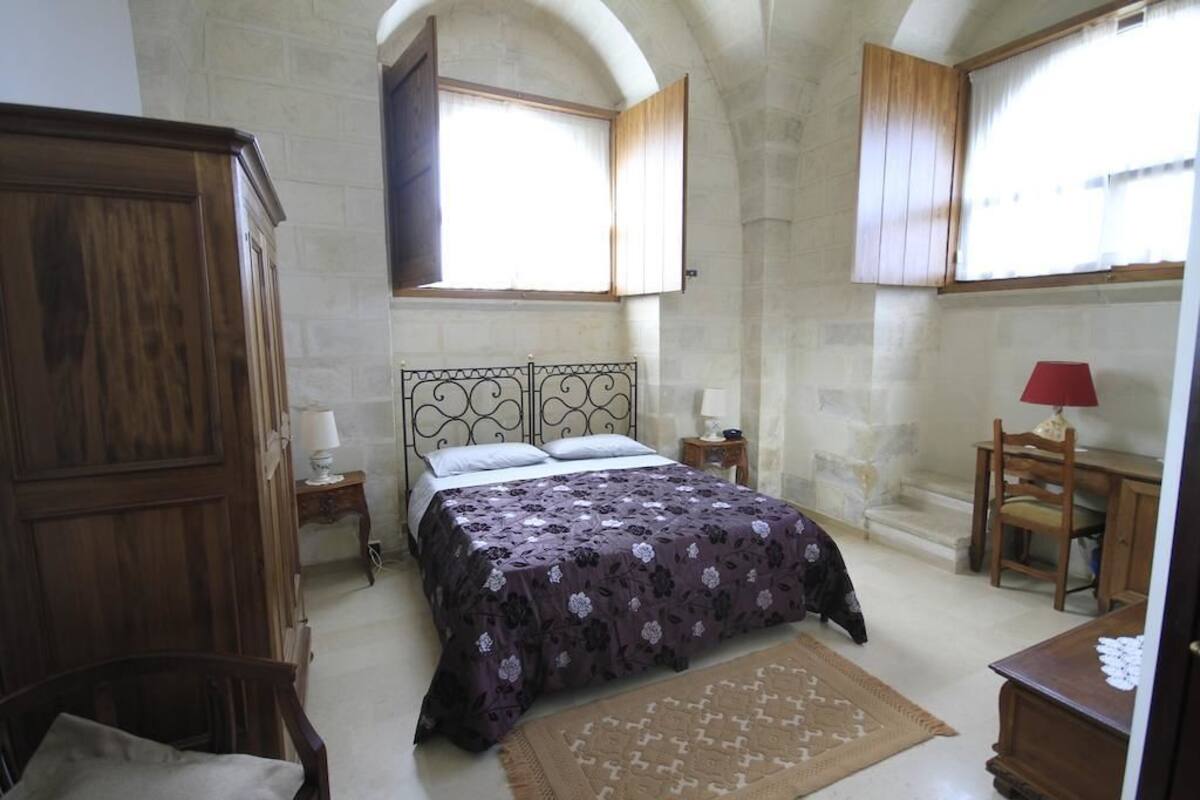 A bedroom with a bed, wooden wardrobe, and a desk with a chair.