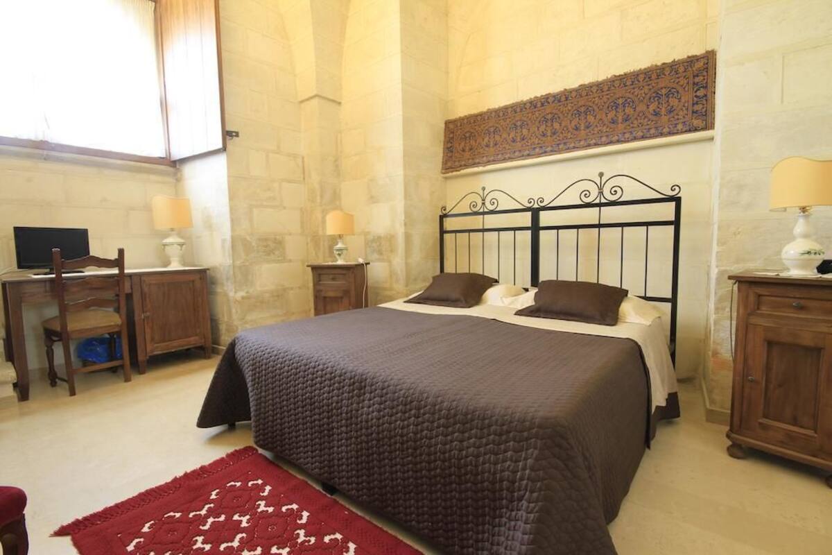 A bedroom with a bed, a desk, a chair, and a lamp.