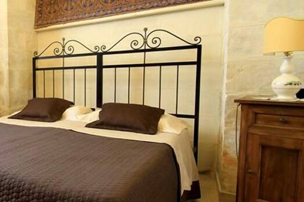 A bedroom with a bed, two bedside tables, a chair, a television, and a decorative wall piece.