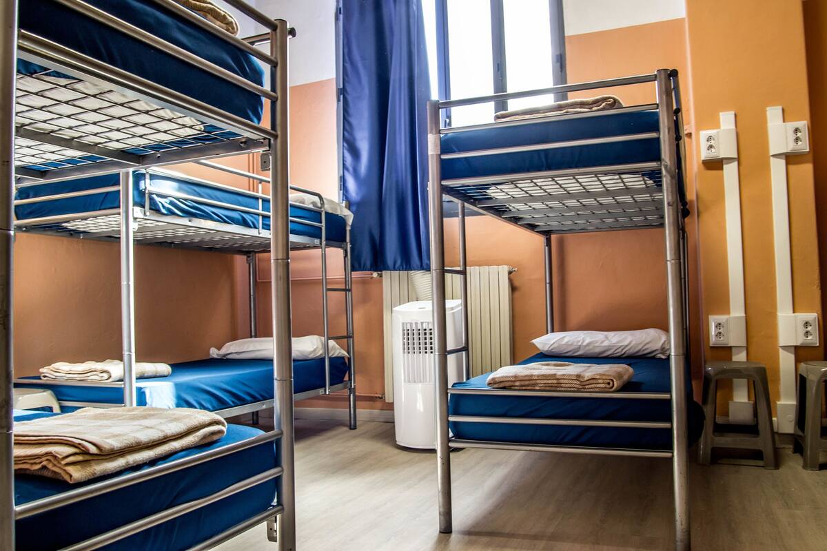 A dormitory room with bunk beds, a heater, and a window with curtains.