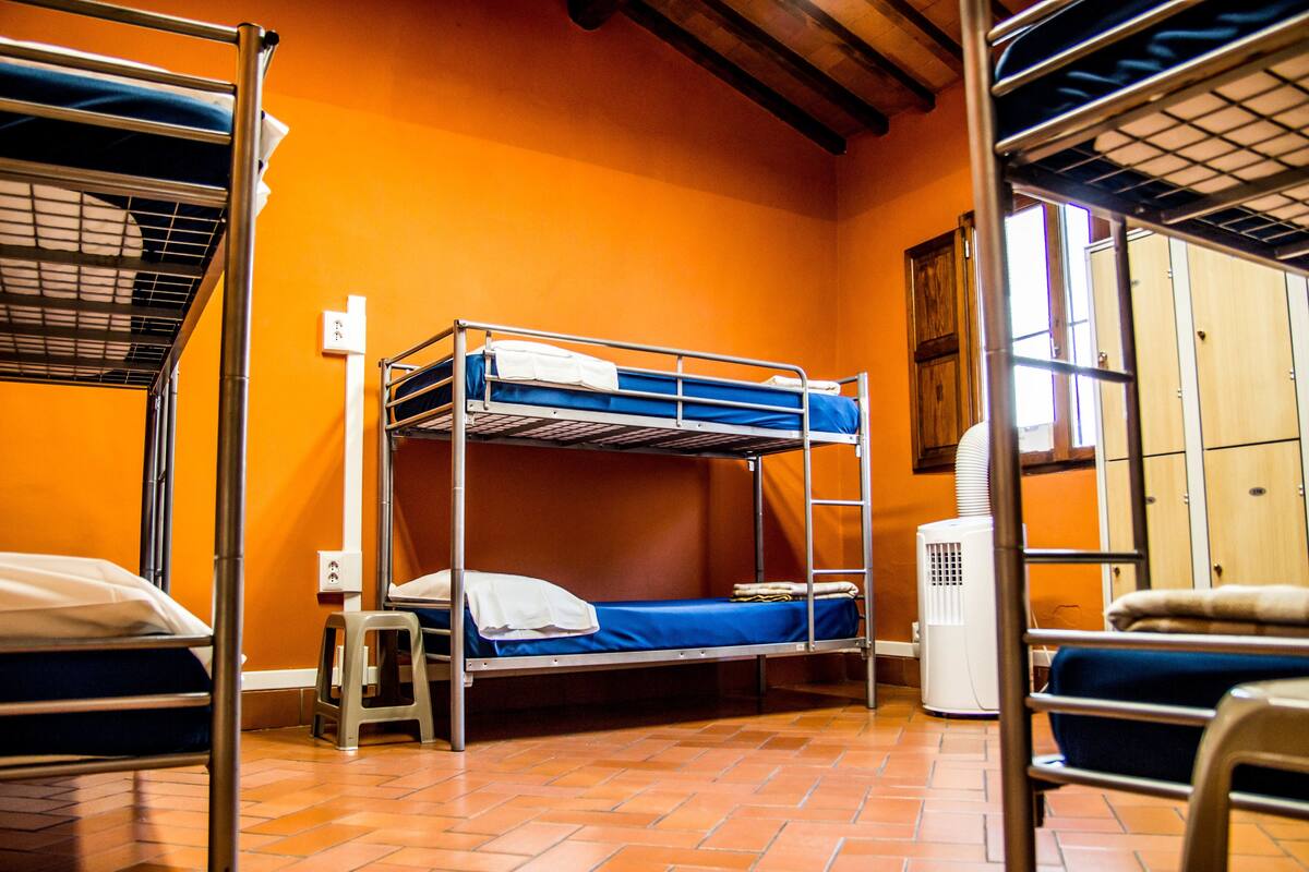 A dormitory room with bunk beds, a heater, and a window.