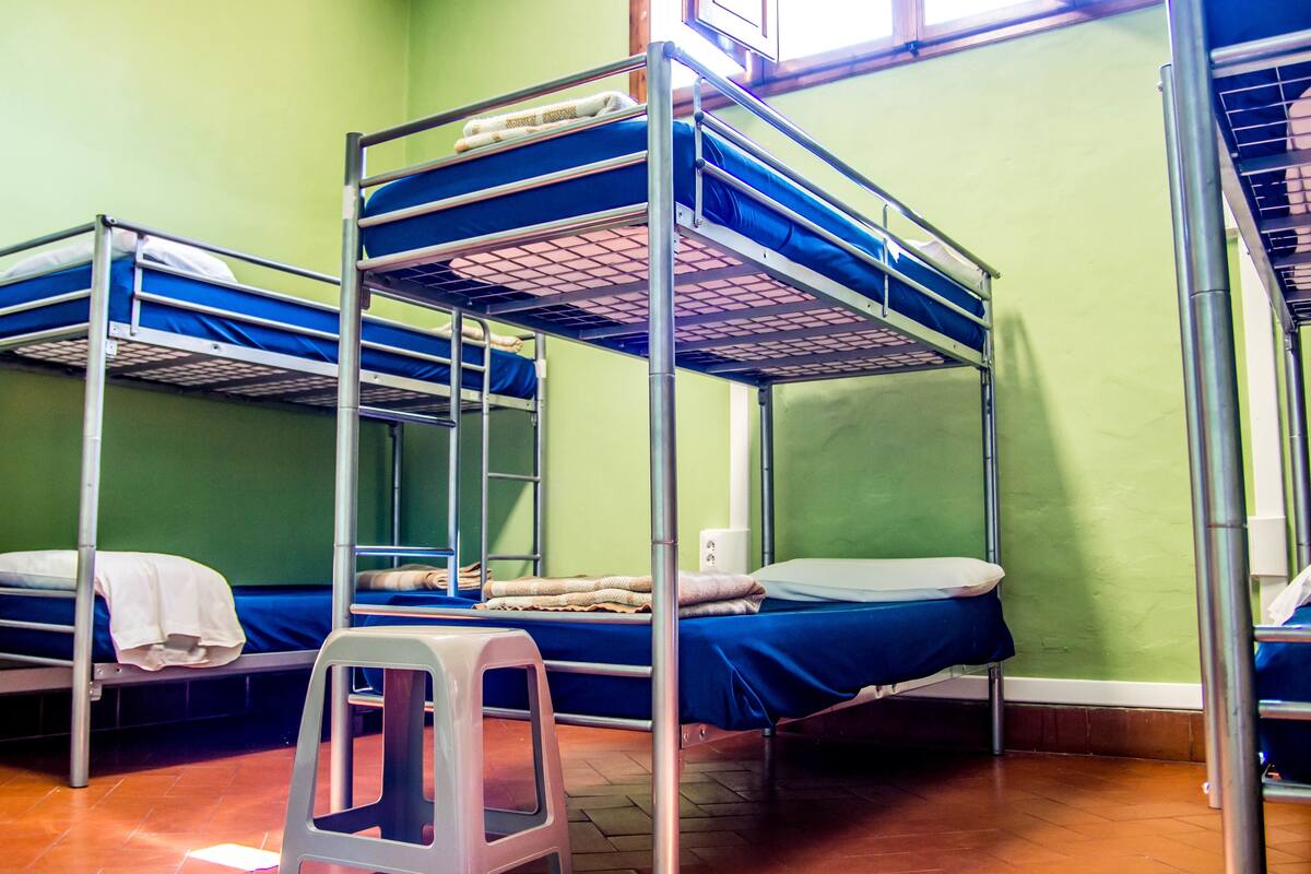 A dormitory room with bunk beds, green walls, and a window.