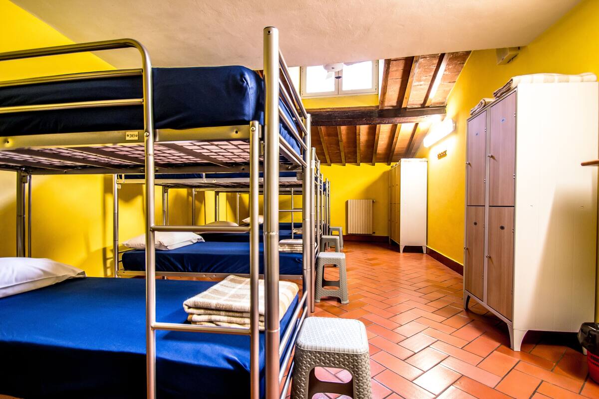 A dormitory room with bunk beds, a small stool, and a refrigerator.