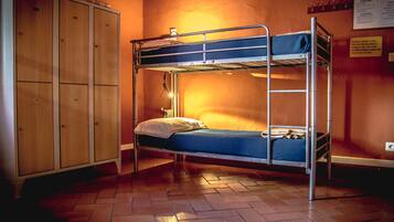 Dormitorio con literas, un armario de madera y una lámpara fijada a la pared.
