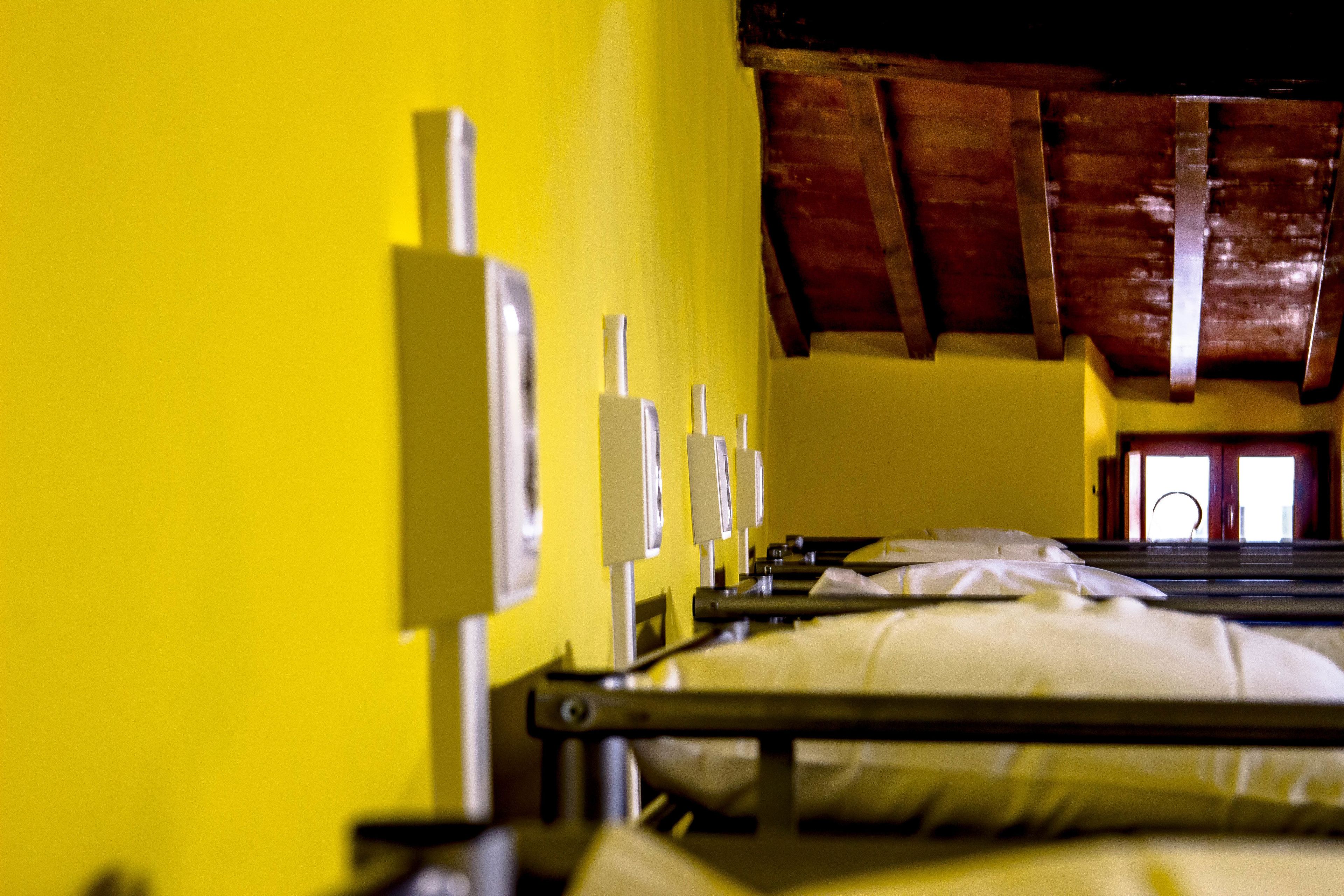 Una habitación con paredes amarillas, vigas de madera en el techo y una cama con ropa blanca.