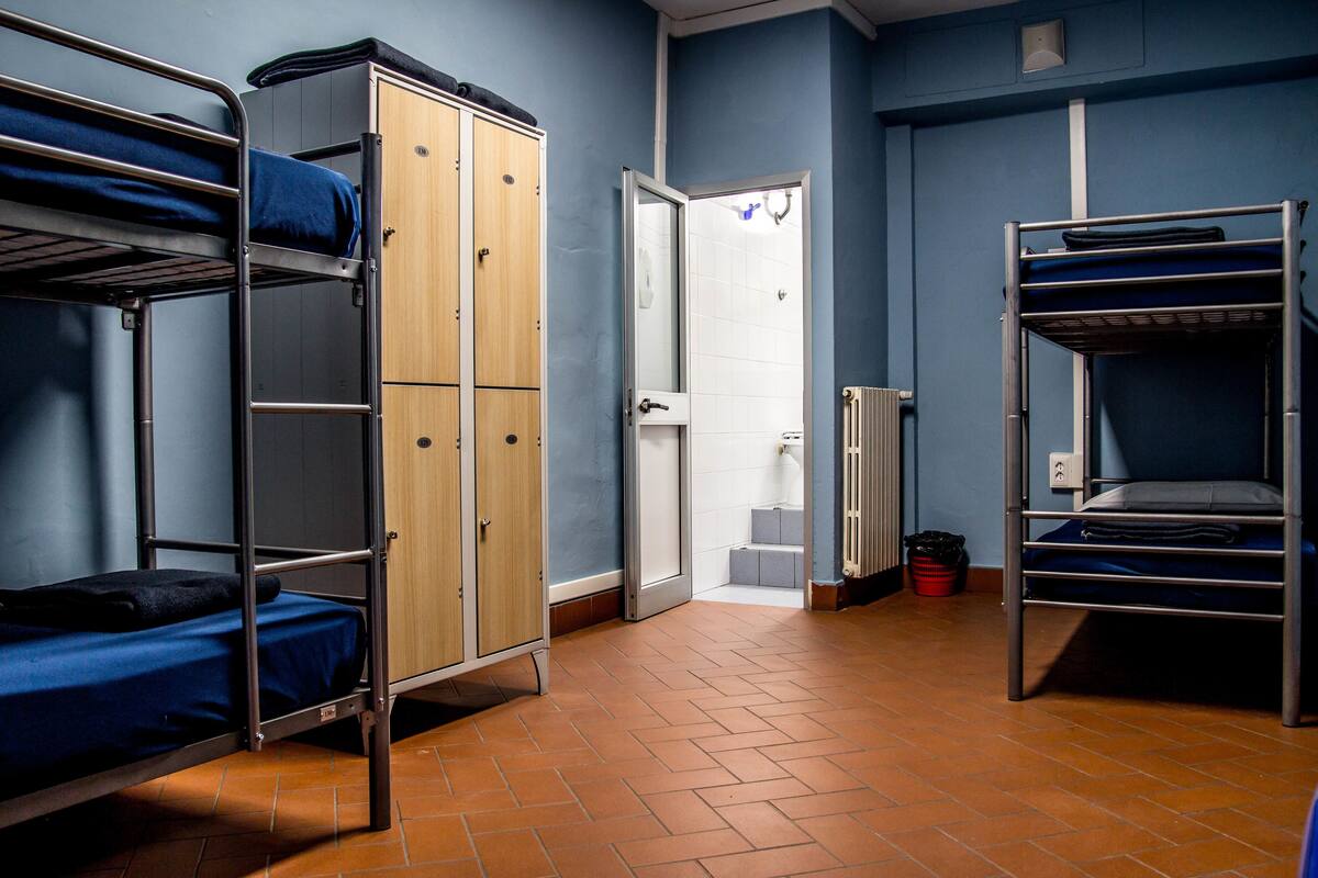 A dormitory room with bunk beds, a wardrobe, and a bathroom door.