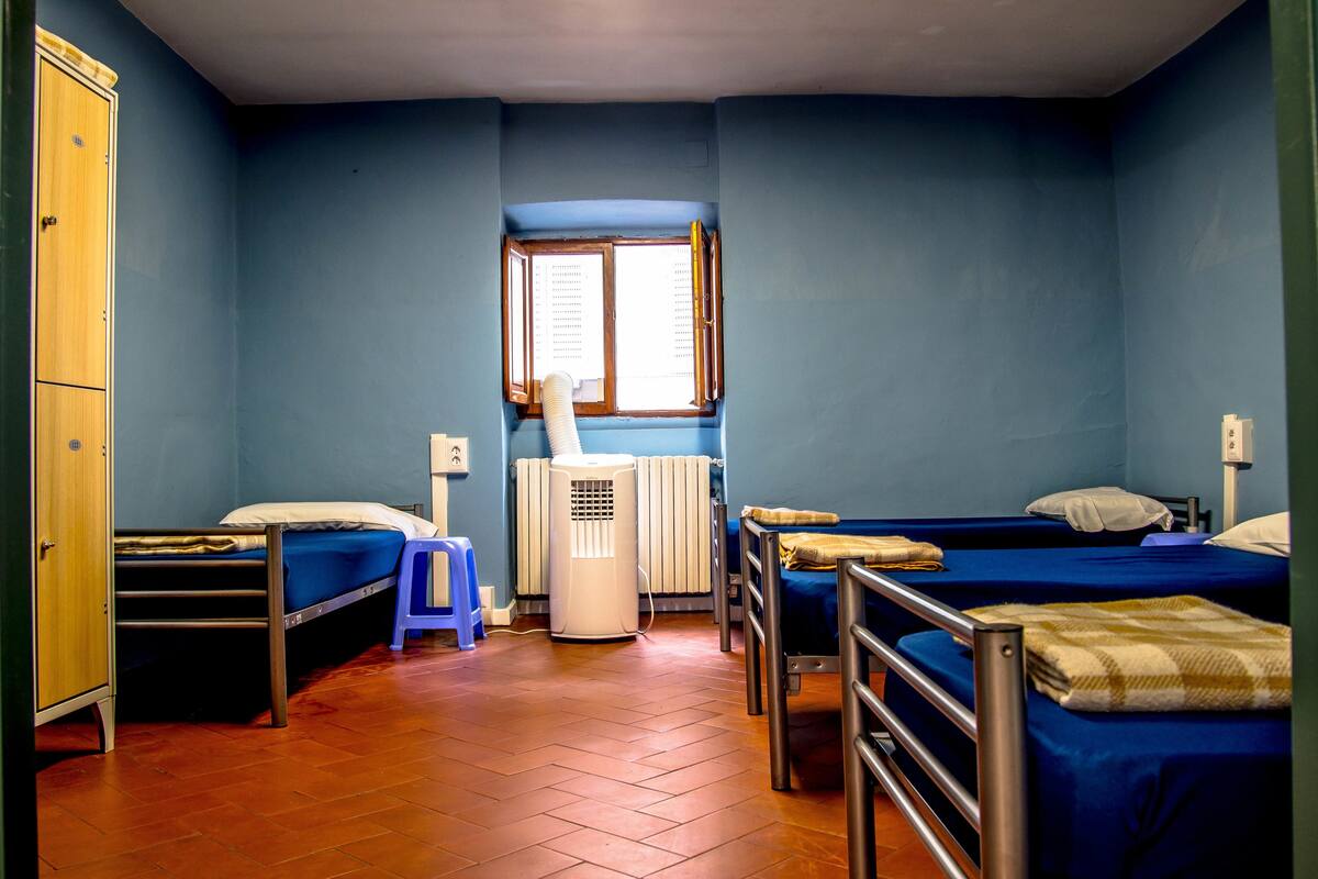 A dormitory room with two beds, a radiator, a window, and a wardrobe.